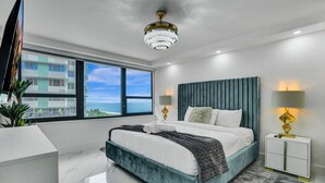 A modern bedroom with a large bed, a view of the ocean, and a chandelier. - Cozy Ocean View Condo / Beach Service & Pool /808 (Miami Beach)