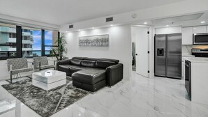 A modern living room with a black leather sofa, a glass coffee table, and a patterned rug. - Cozy Ocean View Condo / Beach Service & Pool /808 (Miami Beach)