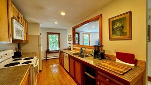 A kitchen with wooden cabinets, a microwave, a stove, a sink, and a large mirror. - High Street Haven, steps to Camden Harbor (Camden)