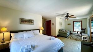 Quarto de hotel com cama, escrivaninha, cadeira, sofá, ventoinha no teto e janela.