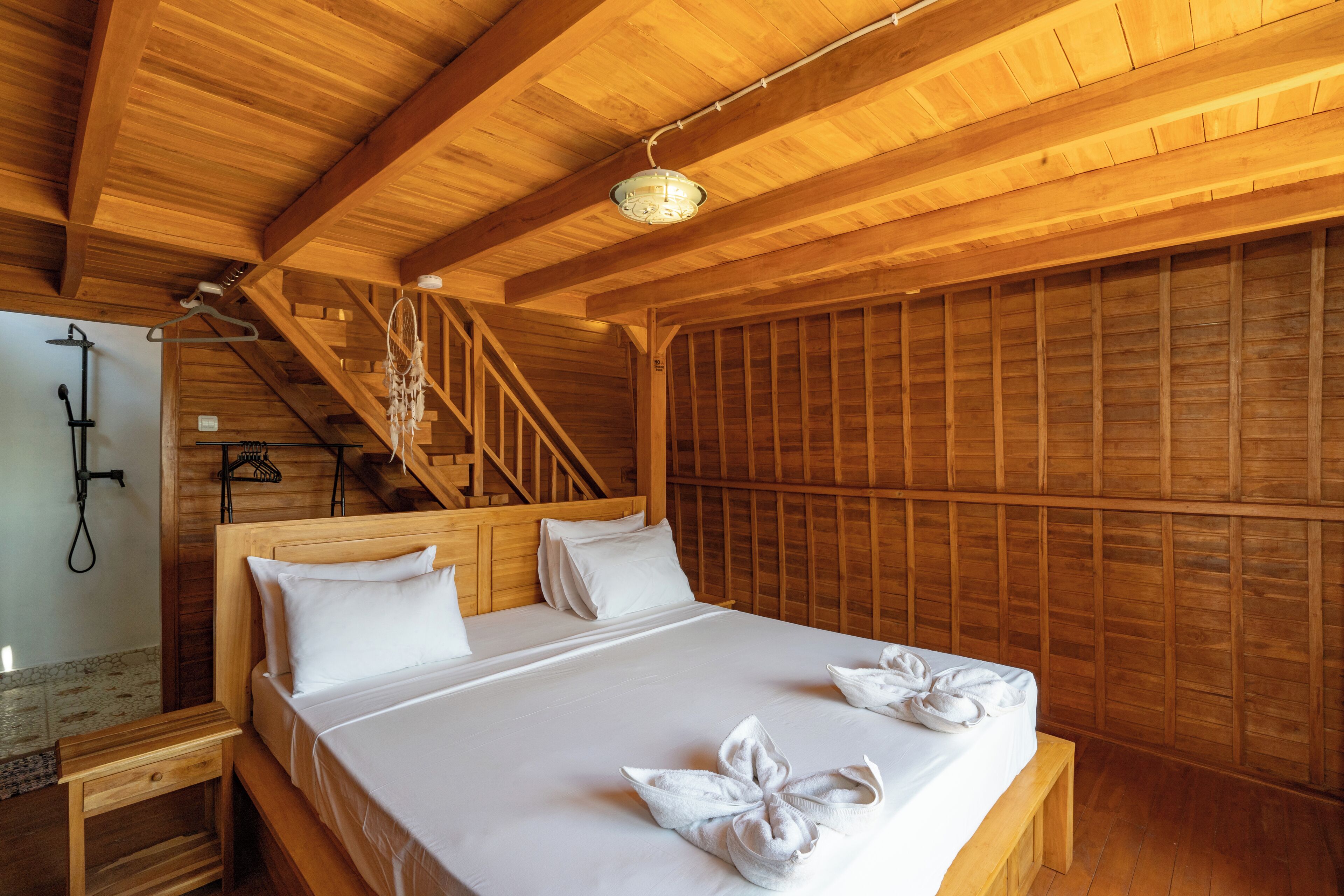 A wooden cabin room with a bed, a wooden bench, a staircase, and a hanging light fixture.