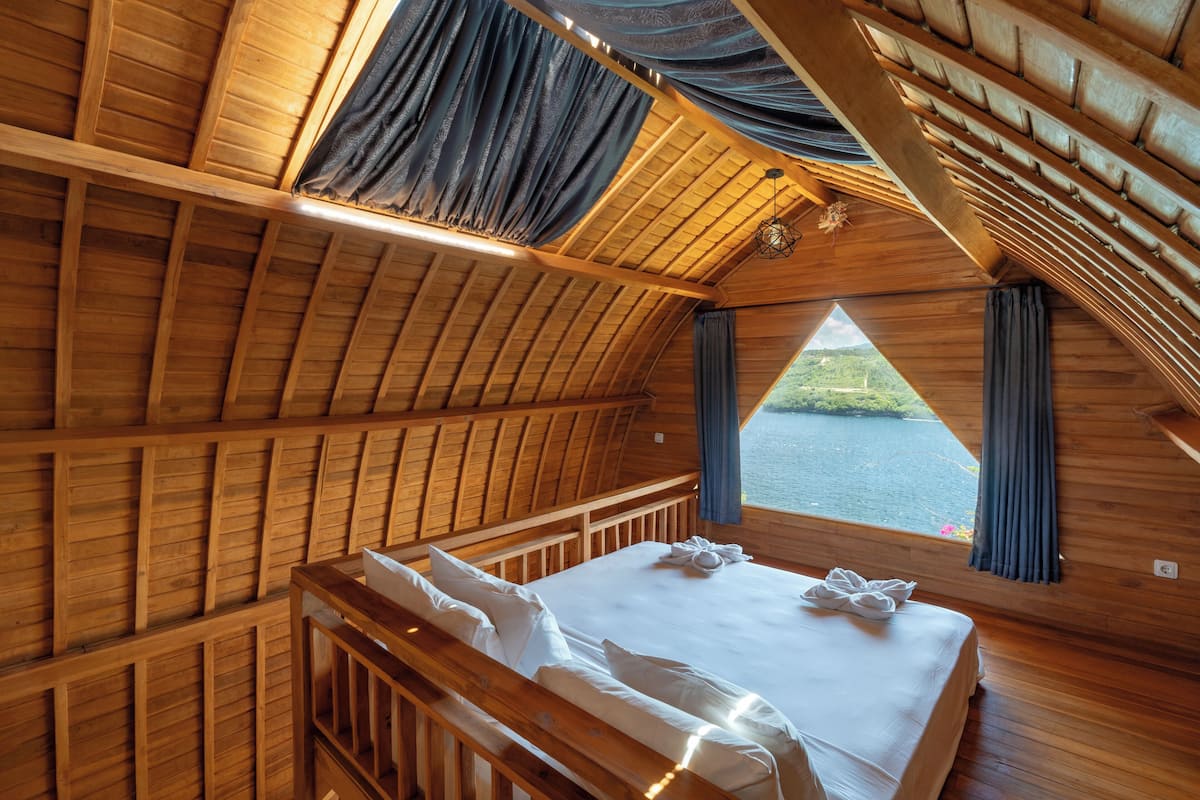 Uma cabana de madeira com cama, cortinas e vista para um lago.