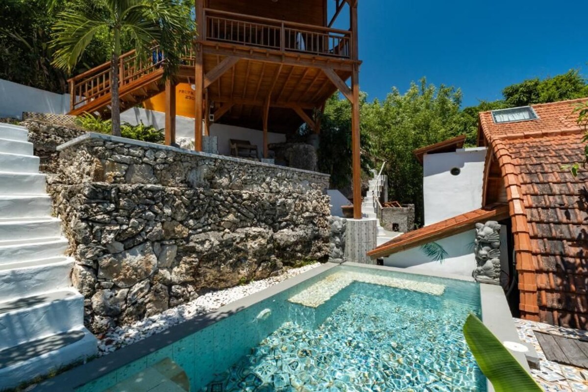 Un muro de piedra, una piscina con agua cristalina y una terraza de madera.
