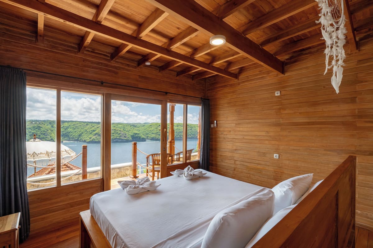 Quarto de cabana de madeira com uma cama grande, vista para um lago e varanda com móveis de madeira.