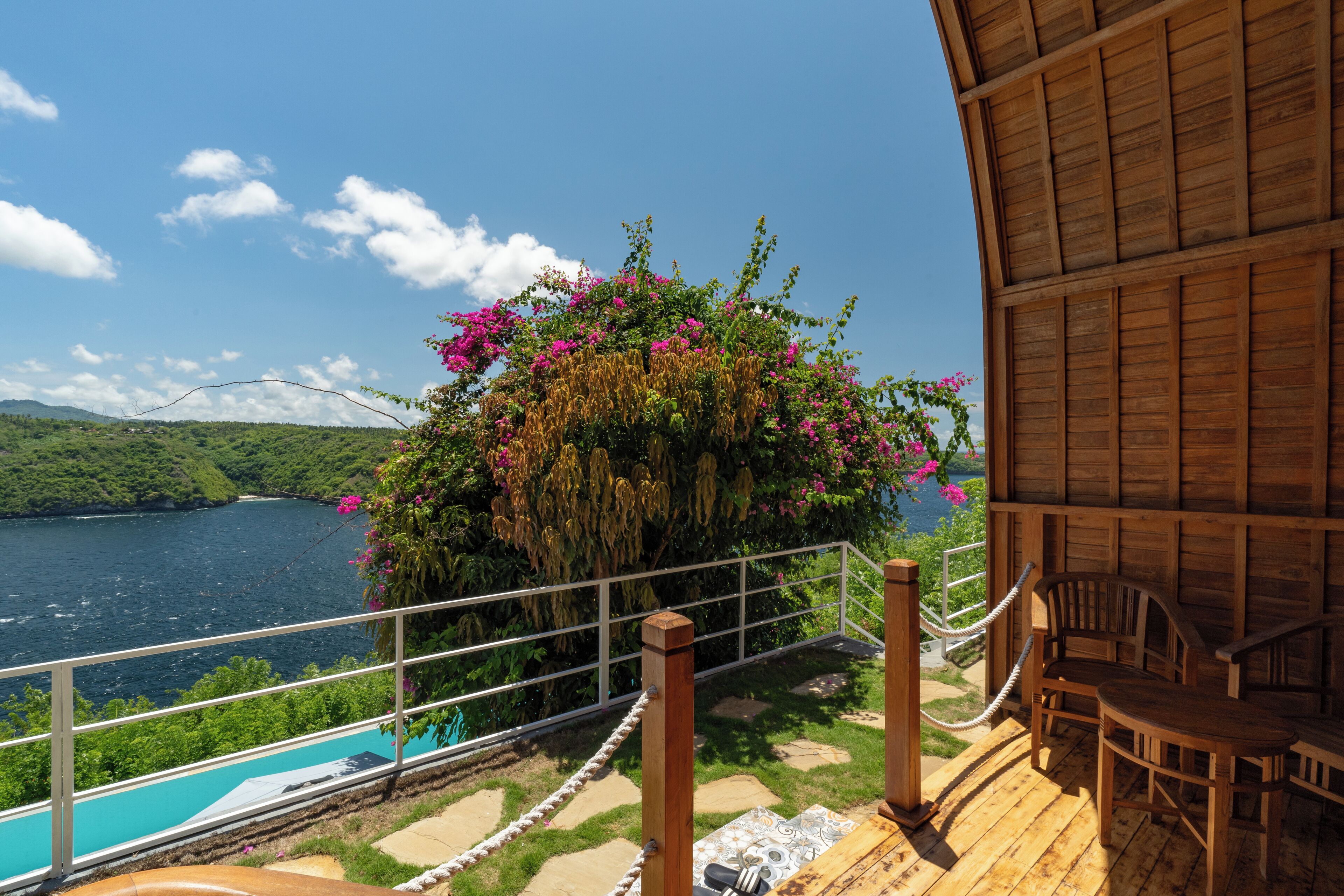 A wooden deck with a pool, overlooking a lake and lush greenery.