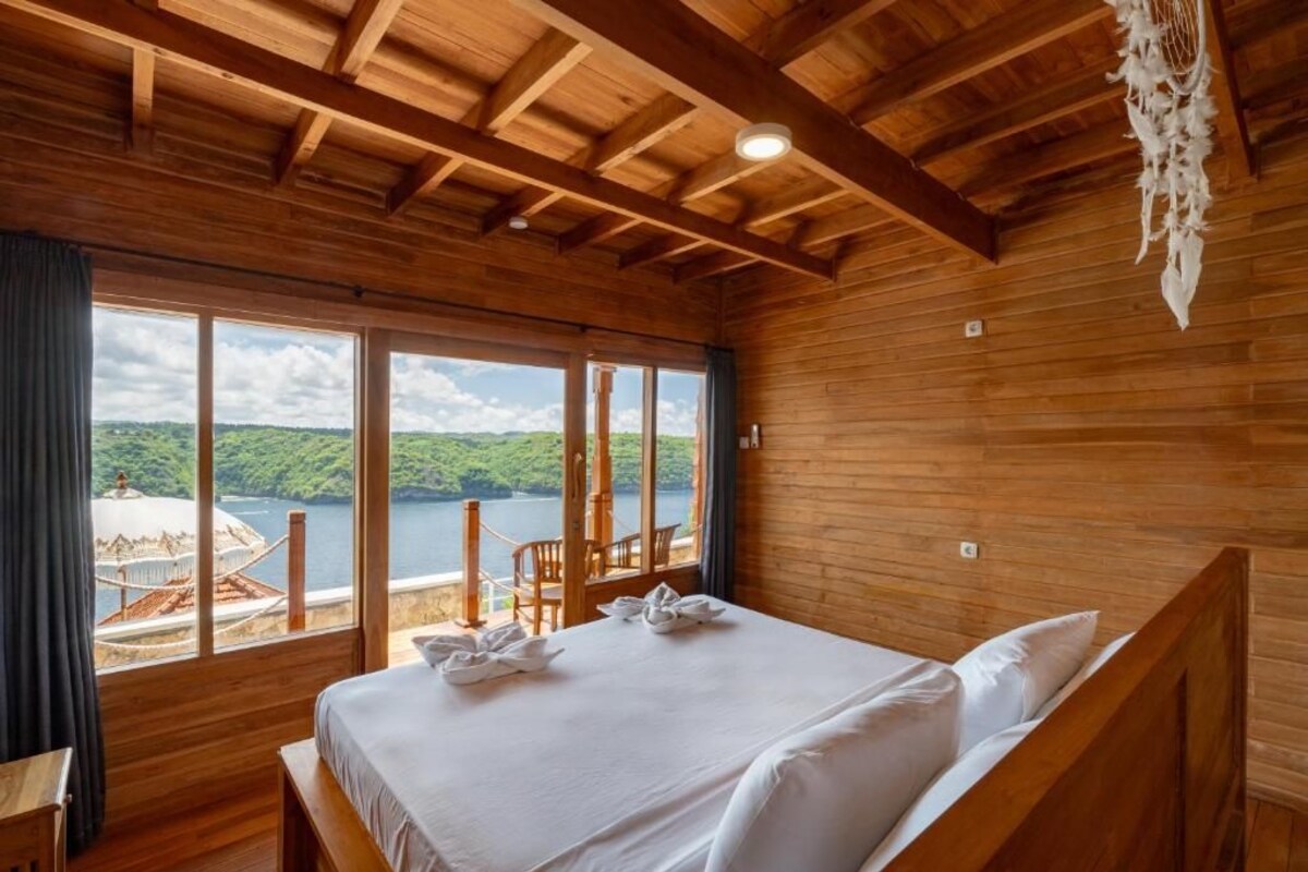 Una habitación de madera con cama, ventanas amplias y vista a un lago.