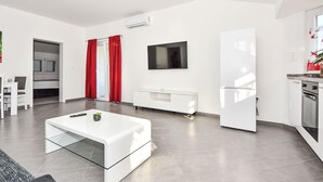 A modern living room with a white sofa, a glass coffee table, and a flat-screen TV mounted on the wall. - Apartment Zubčić by Interhome (Sv. Filip i Jakov)
