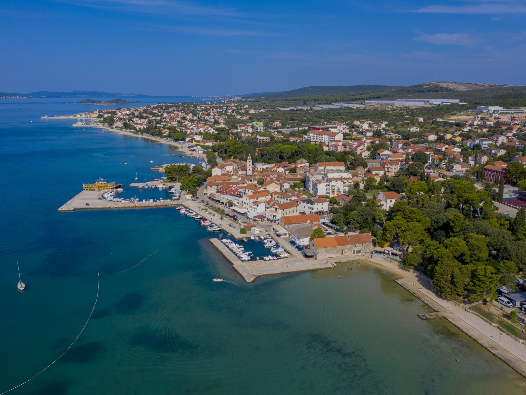 An aerial view of a coastal town with a marina, residential buildings, and a prominent church.