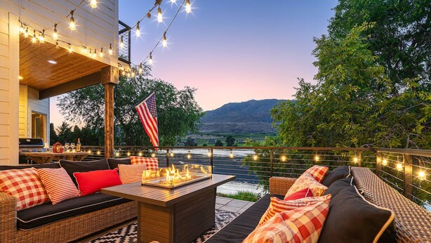 Un patio con mobiliario exterior, una fogata, luces colgantes y una bandera estadounidense.