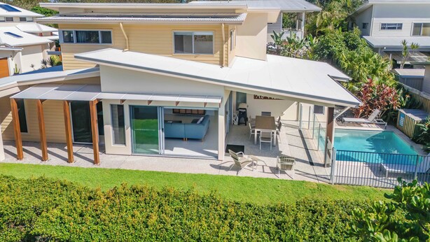 Una casa moderna de dos pisos con un patio cubierto, una piscina y un césped bien cuidado.