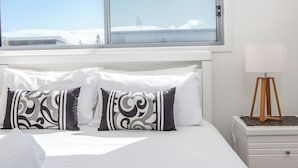 Un dormitorio con una cama, almohadas blancas, una lámpara de noche y una ventana con vistas a un paisaje nevado.