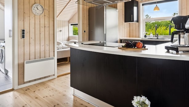 Une cuisine moderne dotée d’un îlot central, de murs en bois, d’un four encastré et d’une fenêtre donnant sur un paysage verdoyant.