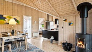 Un espace de vie moderne à aire ouverte, comprenant une cuisine centrale, un coin repas et un poêle à bois.