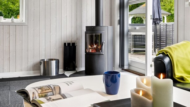 A modern interior with a wood-burning stove, a window with a view of greenery, and a cozy seating area with candles and a book. - "Tayana" - 700m from the sea by Interhome (Sydals)