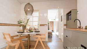 Une cuisine moderne avec un coin repas, comprenant une table ronde, des chaises en bois et un luminaire suspendu en fibres tressées.