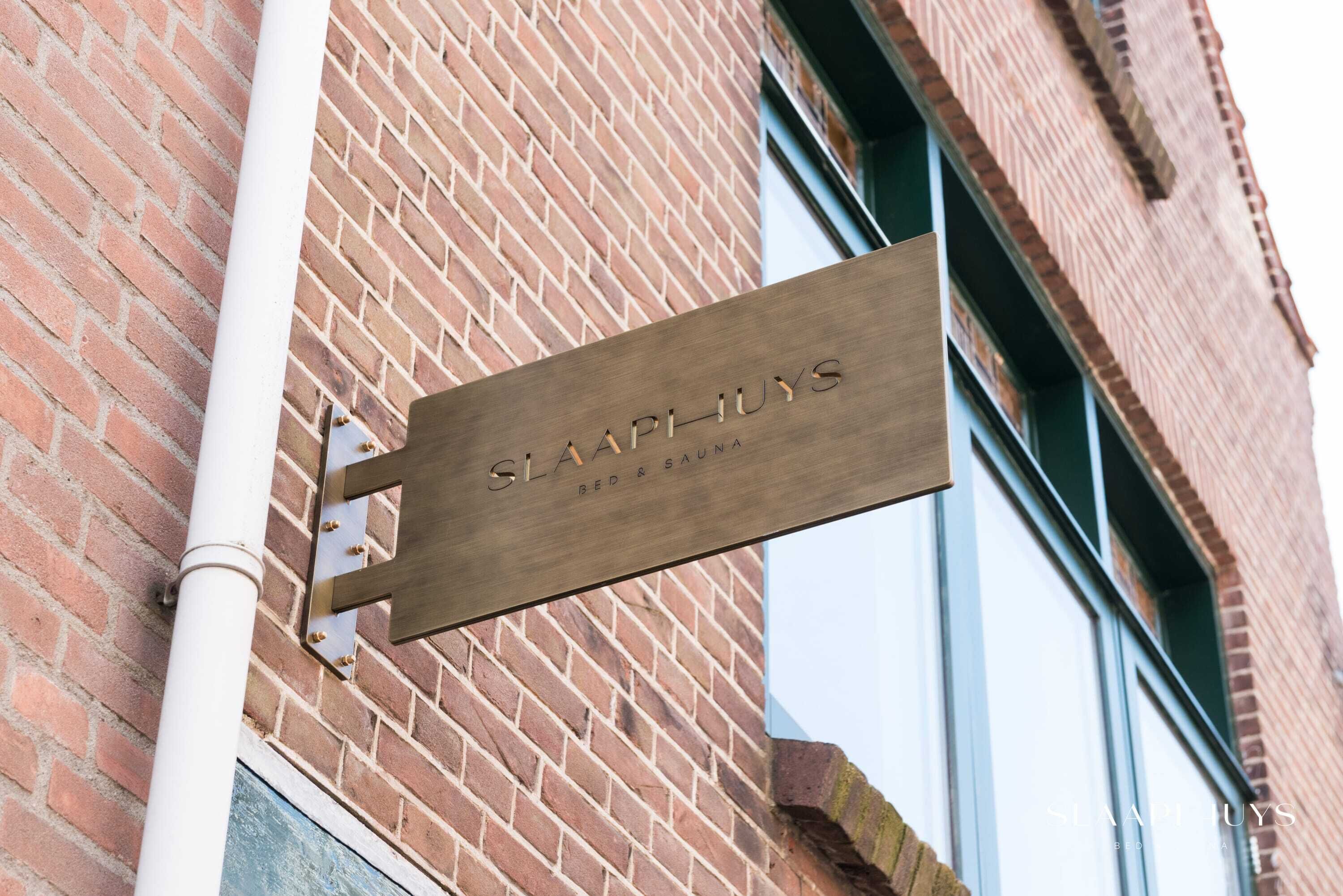 A sign for 'SLAPHIYUS BED & SAUN' mounted on a brick wall.