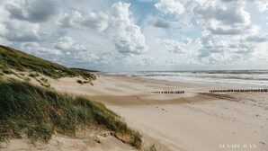 Une plage avec des dunes de sable et une jetée en bois qui s’avance dans la mer.