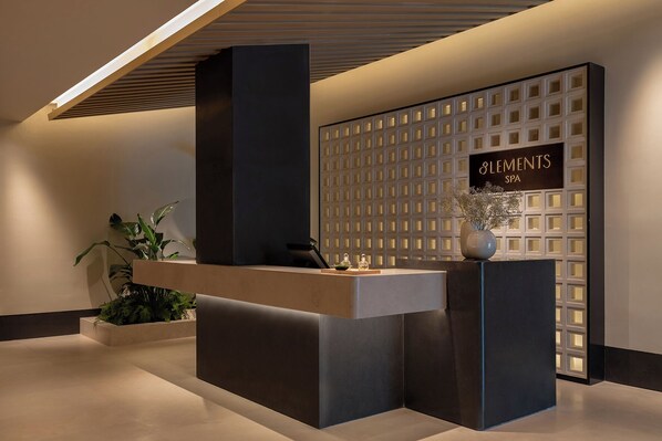 Un espace d’accueil au design moderne, comprenant un comptoir de réception, un mur orné d’un motif en réseau et une enseigne indiquant « ELEMENTS SPA ».