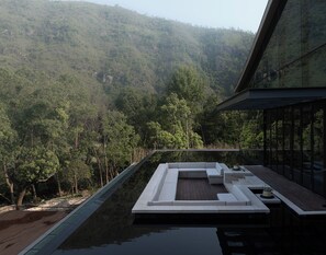 Un espace piscine extérieur moderne, doté d’un coin salon et offrant une vue sur une colline boisée.