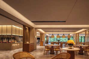 A modern dining area with a central round table, surrounded by wicker chairs, and a kitchen area with a counter and appliances. - Garrya Xianju (Taizhou)