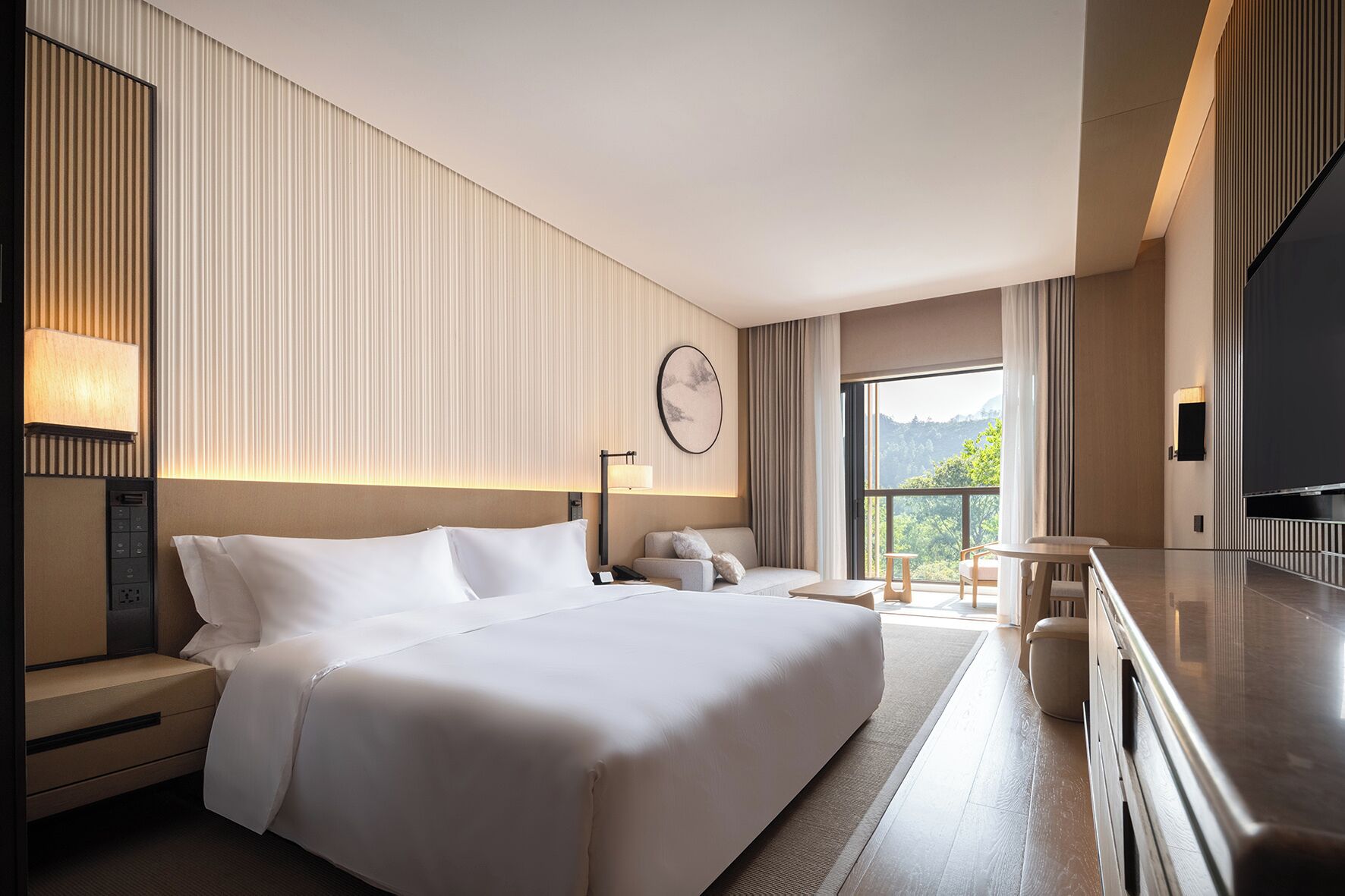 Habitación de hotel moderna con una cama grande, un escritorio, una silla, un televisor y un balcón con vistas.