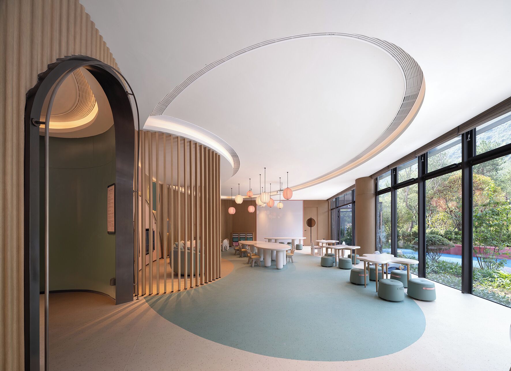 Ein modernes Interieur mit gewölbter Decke, großen Fenstern und einer Sitzecke mit Tischen und Stühlen.