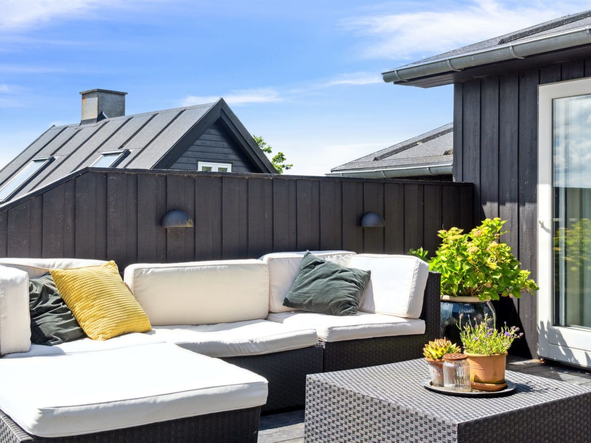 An outdoor seating area with a sofa and two side tables, a potted plant, and a window with a view of a building.