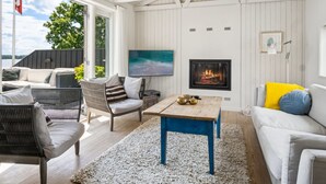 A modern living room with a fireplace, comfortable seating, and a large window overlooking a body of water. - "Sten" - 30m from the sea by Interhome (Bjert)