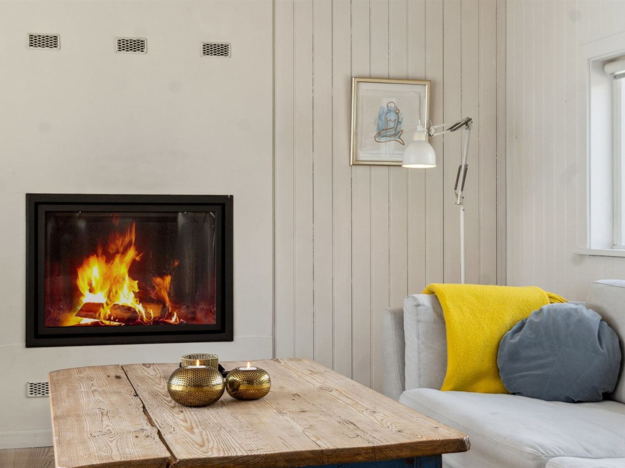 A room with a fireplace, a framed picture on the wall, a table with candles, and a sofa with cushions.