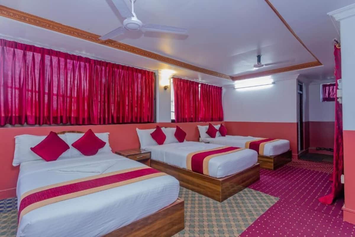 A hotel room with three beds, red curtains, a ceiling fan, and a patterned carpet.