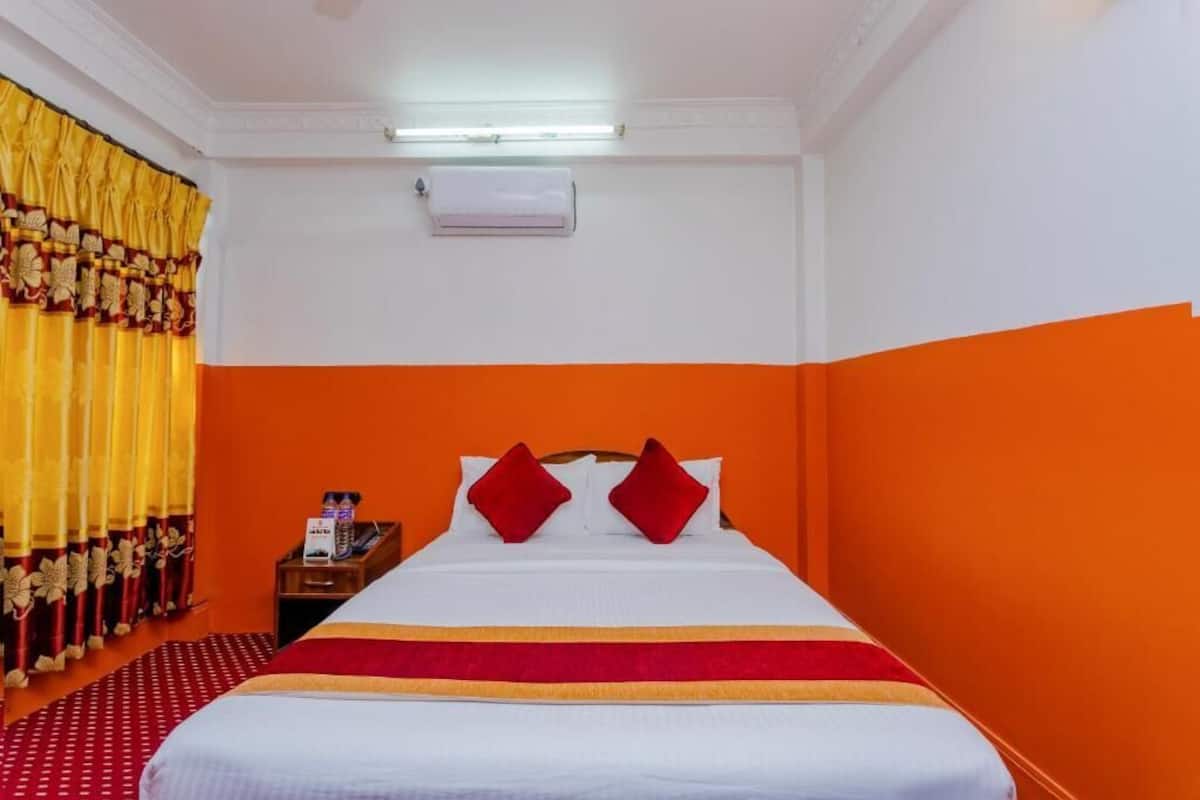 A hotel room with a bed, an air conditioning unit, a nightstand, and a telephone.