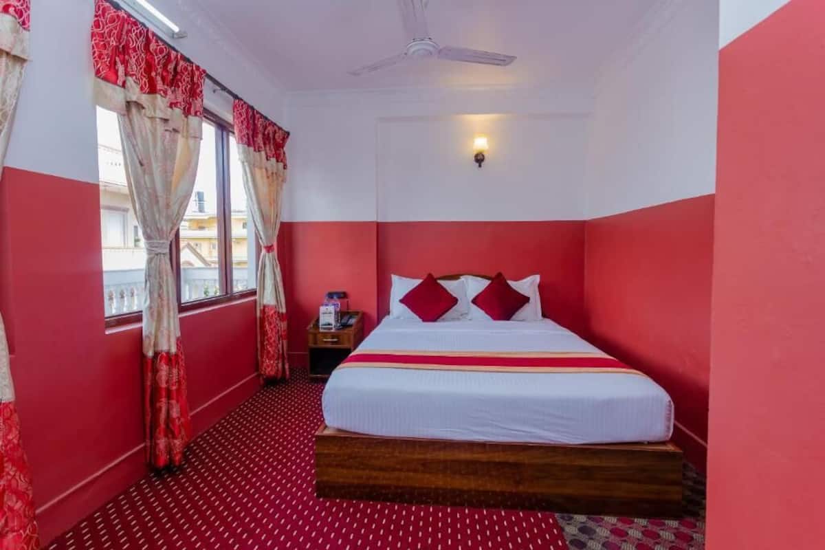 A hotel room with a bed, a nightstand, a ceiling fan, and a window with curtains.