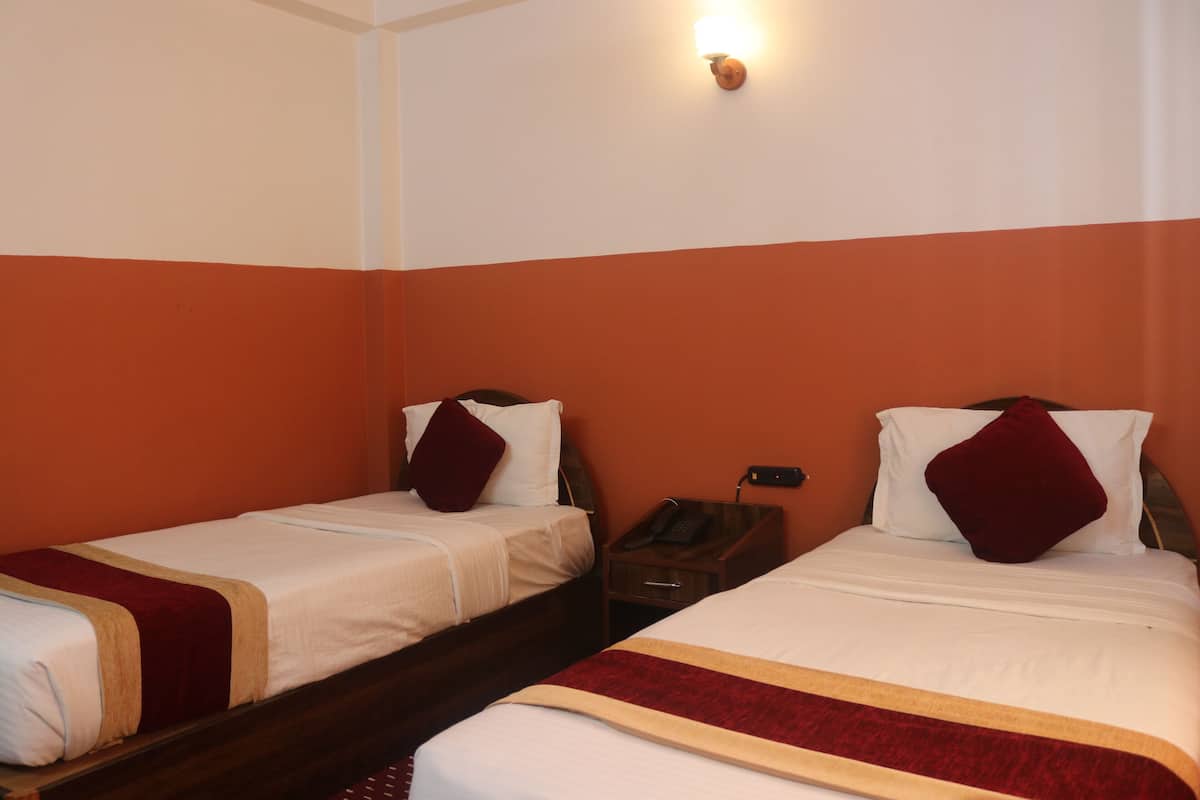 A hotel room with two single beds, each with a red and white bedspread, a wooden nightstand with a telephone, and a wall-mounted light fixture.