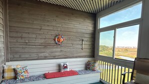 A covered porch with a bench, a decorative wall piece, and a view of a natural landscape.
