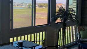 A room with large windows, a chair, a small table, and a potted plant.