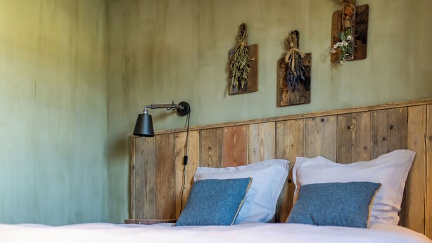 A bedroom with a wooden headboard, two pillows, a bedside lamp, and wall-mounted decorations.
