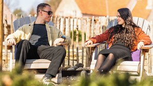 Two people sitting on wooden chairs outdoors.
