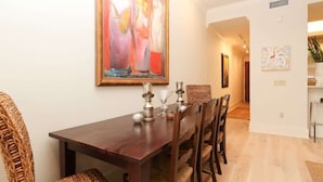 A dining area with a wooden table and wicker chairs, a painting on the wall, and a hallway leading to another room.