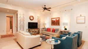 A modern living room with a sofa, armchairs, a TV, and a ceiling fan.