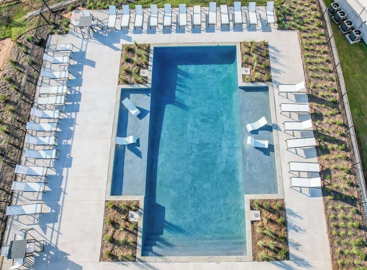 Vue aérienne d’une piscine rectangulaire entourée d’une terrasse, de chaises longues et de petits espaces paysagers.