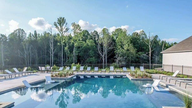 Una piscina rectangular con agua azul cristalina, rodeada de sillones blancos y una valla.