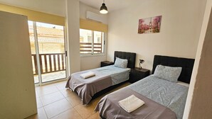 Quarto com duas camas, varanda, um quadro e mesa de cabeceira com abajur.