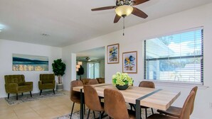 A dining area with a wooden table, brown chairs, a ceiling fan, and artwork on the walls.