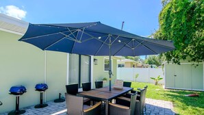 An outdoor patio with a table and chairs, a large umbrella, and two barbecue grills.