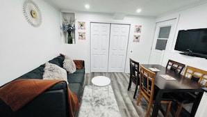 A living room with a sofa, a dining table, chairs, a TV, and a wardrobe. - Cozy 2 Bedroom Apartment near St.John's airport with lockbox key Entrance. (St. John's)