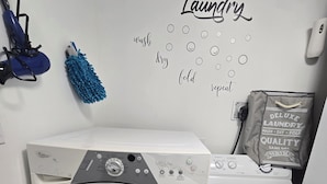 A front-loading washing machine and dryer in a laundry room with a wall-mounted drying rack and a wall decal with laundry-related words. - Cozy 2 Bedroom Apartment near St.John's airport with lockbox key Entrance. (St. John's)