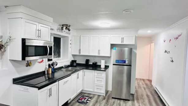 A modern kitchen with white cabinetry, a stainless steel refrigerator, and a microwave. - Cozy 2 Bedroom Apartment near St.John's airport with lockbox key Entrance. (St. John's)
