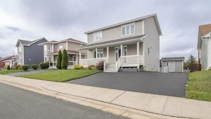 A two-story residential building with a front porch, a driveway, and a well-maintained lawn. - Cozy 2 Bedroom Apartment near St.John's airport with lockbox key Entrance. (St. John's)