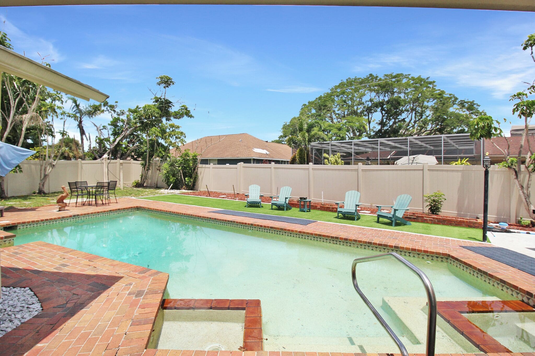 A swimming pool with a brick deck, surrounded by a fence and trees.