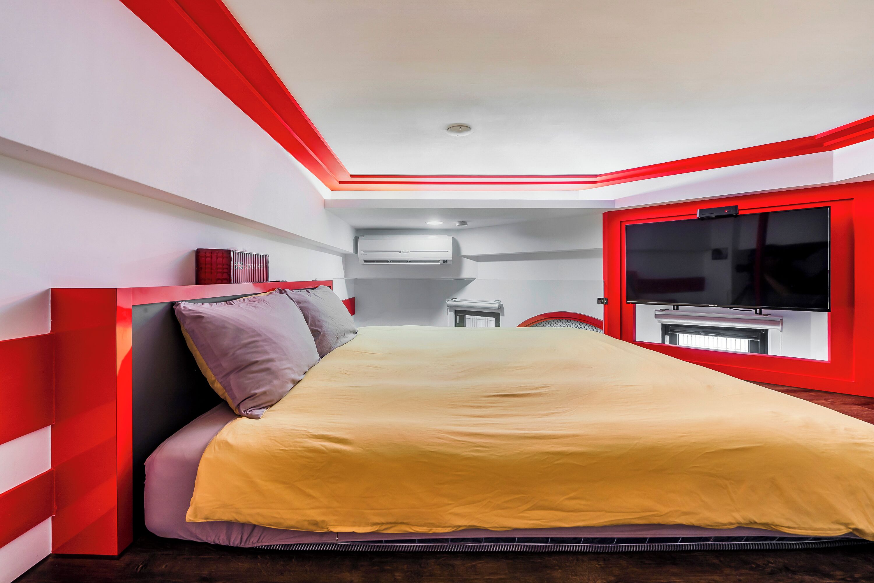 A modern bedroom with a bed, a TV, and a red-framed window.